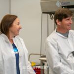 Two people in lab coats smiling during a tour of a Germfree facility.