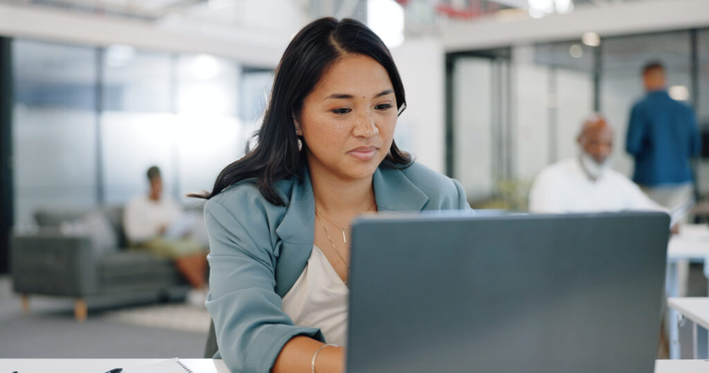 Woman focused on working at a laptop in a modern office setting.