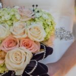 Bridal bouquet with white and peach roses, green hydrangeas, and decorative details on a wedding dress.