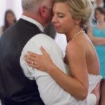 Father-daughter dance at a wedding, bride in white dress and pearls, creating a loving moment.