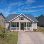 Suburban home with front porch and green lawn under a clear blue sky. Perfect family house.