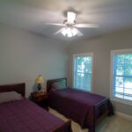 Cozy twin bedroom with purple bedding, ceiling fan, and side window view.