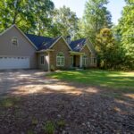 Spacious suburban home with brick facade, two-car garage, and wooded surroundings on a sunny day.