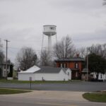 Fayette water tower stands tall over residential homes and trees in a small town setting, overcast sky above.