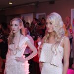 Models in elegant white dresses walking the red carpet at a fashion event.