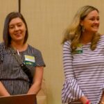 Two women presenters smiling at a conference, wearing name tags.