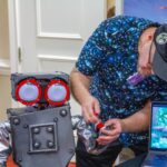 Person adjusting a robotic hand beside a laptop displaying a colorful screen.