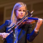 Violinist performing on stage with focused expression and elegant attire.