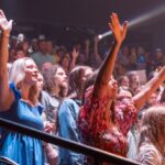 Enthusiastic crowd at a live concert, people raising hands and enjoying the performance.