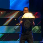 Man holding an illuminated open book on stage with a colorful digital backdrop.