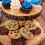 Colorful cupcakes and festive cookies on a rustic wooden stand, perfect for a holiday celebration dessert display.