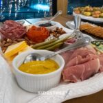 Gourmet charcuterie board with assorted meats, cheeses, pickles, nuts, and mustard dip, perfect for festive gatherings.