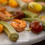 Close-up of a colorful appetizer with shrimp, okra, and cherry tomatoes on a plate.