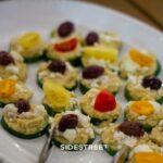 Plate of cucumber bites topped with hummus, feta, olives, and colorful cherry tomatoes, perfect for appetizers.