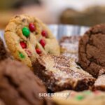 Assorted cookies with colorful candy chips and brownies dusted with powdered sugar on a festive platter.