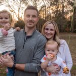 Family smiling outdoors in a backyard during sunset with trees in the background.